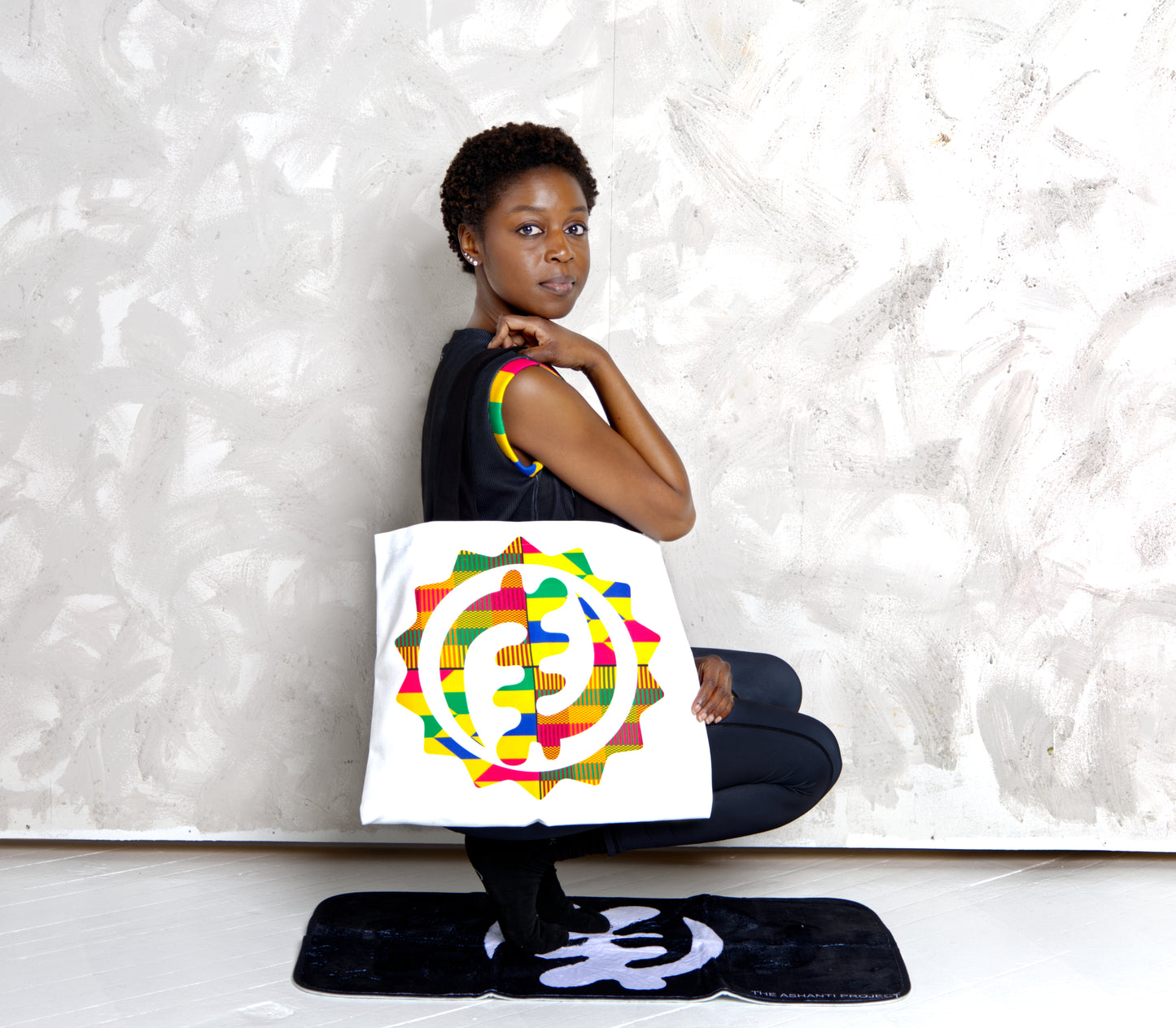 Woman holding a colorful tote bag with a design on a textured white background