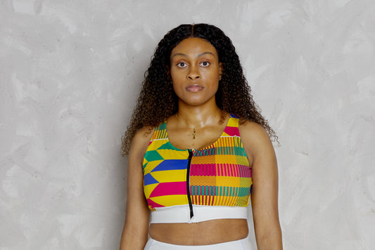 Woman wearing a colorful kente patterned top against a plain background. It’s a padded sports bra with kente designs