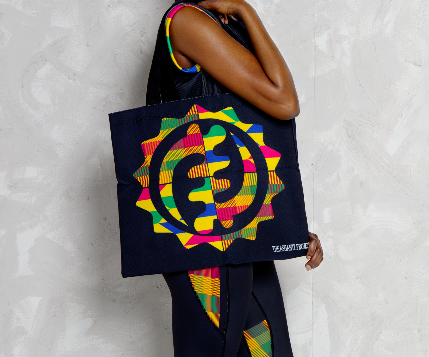 Black woman holding a colorful tote bag with a geometric design on a textured white background
