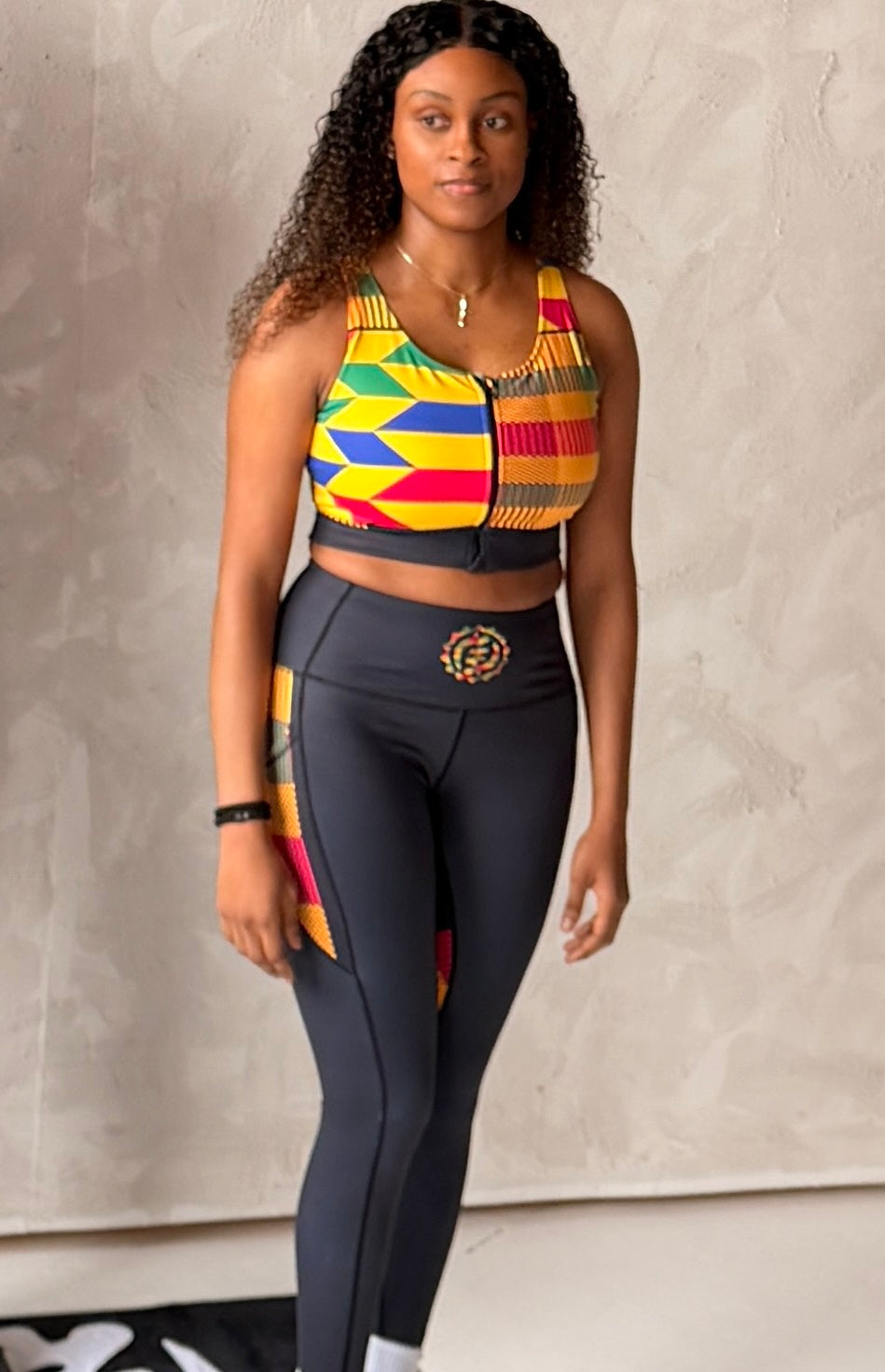Woman wearing a colorful athletic top and black leggings against a neutral background