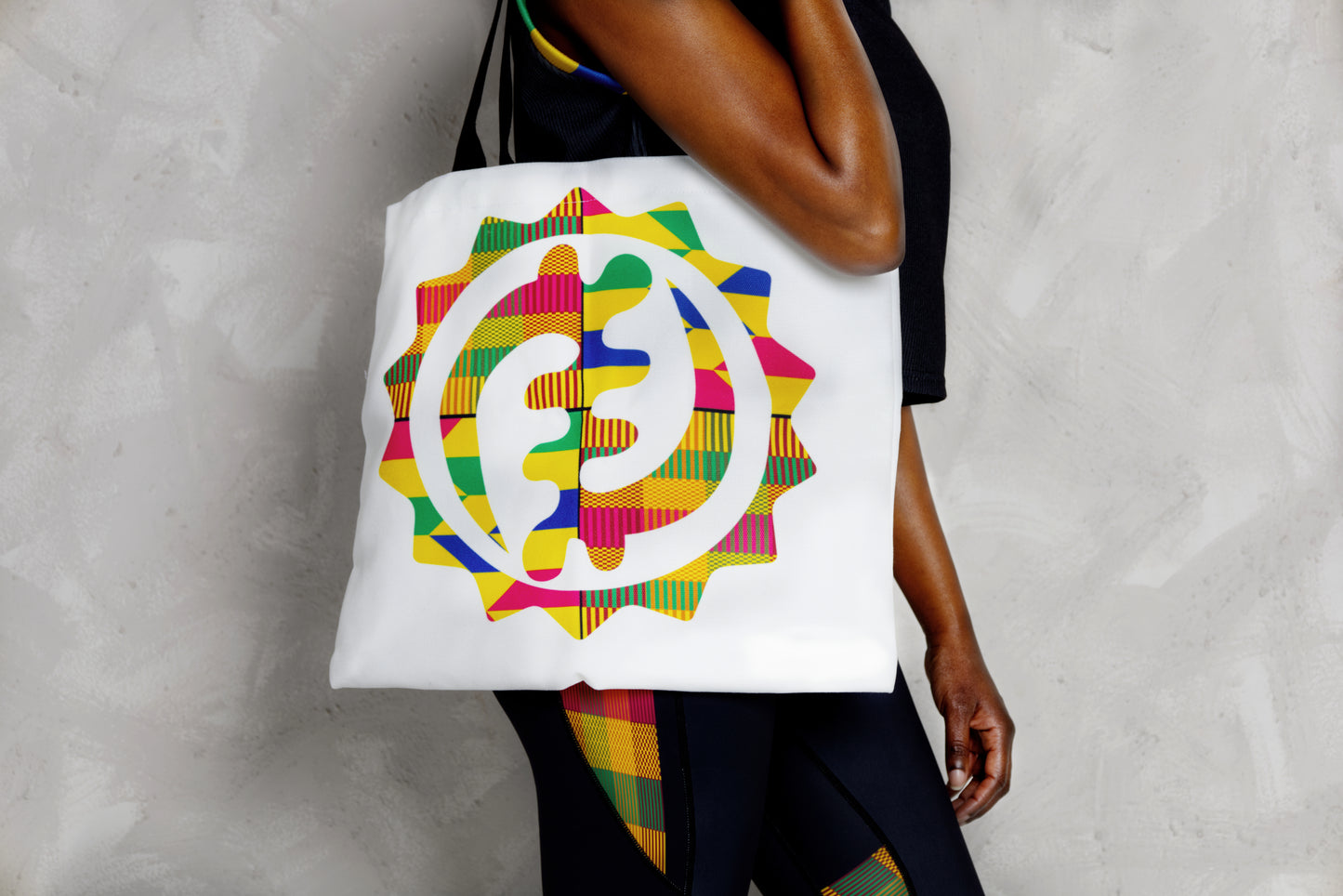 Person holding a colorful tote bag with a geometric design against a neutral background