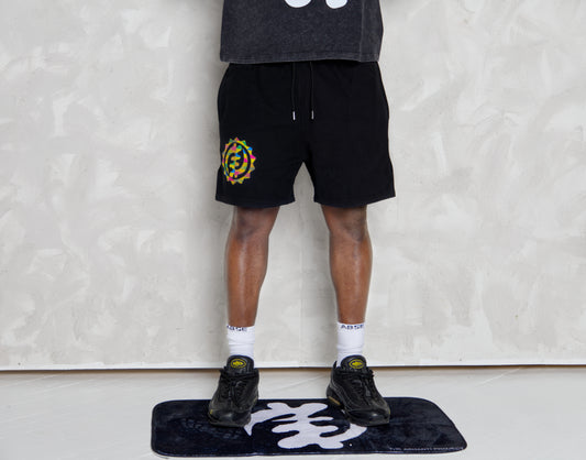 Person wearing black shorts with a colorful logo, standing on a black mat with white design against a plain background.