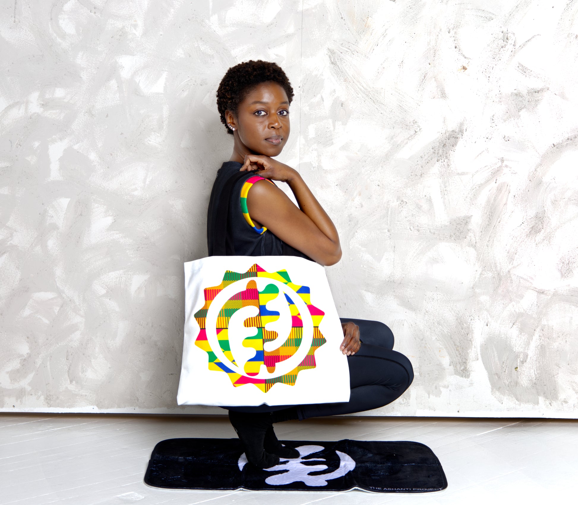 Woman holding a colorful tote bag with a design on a textured white background