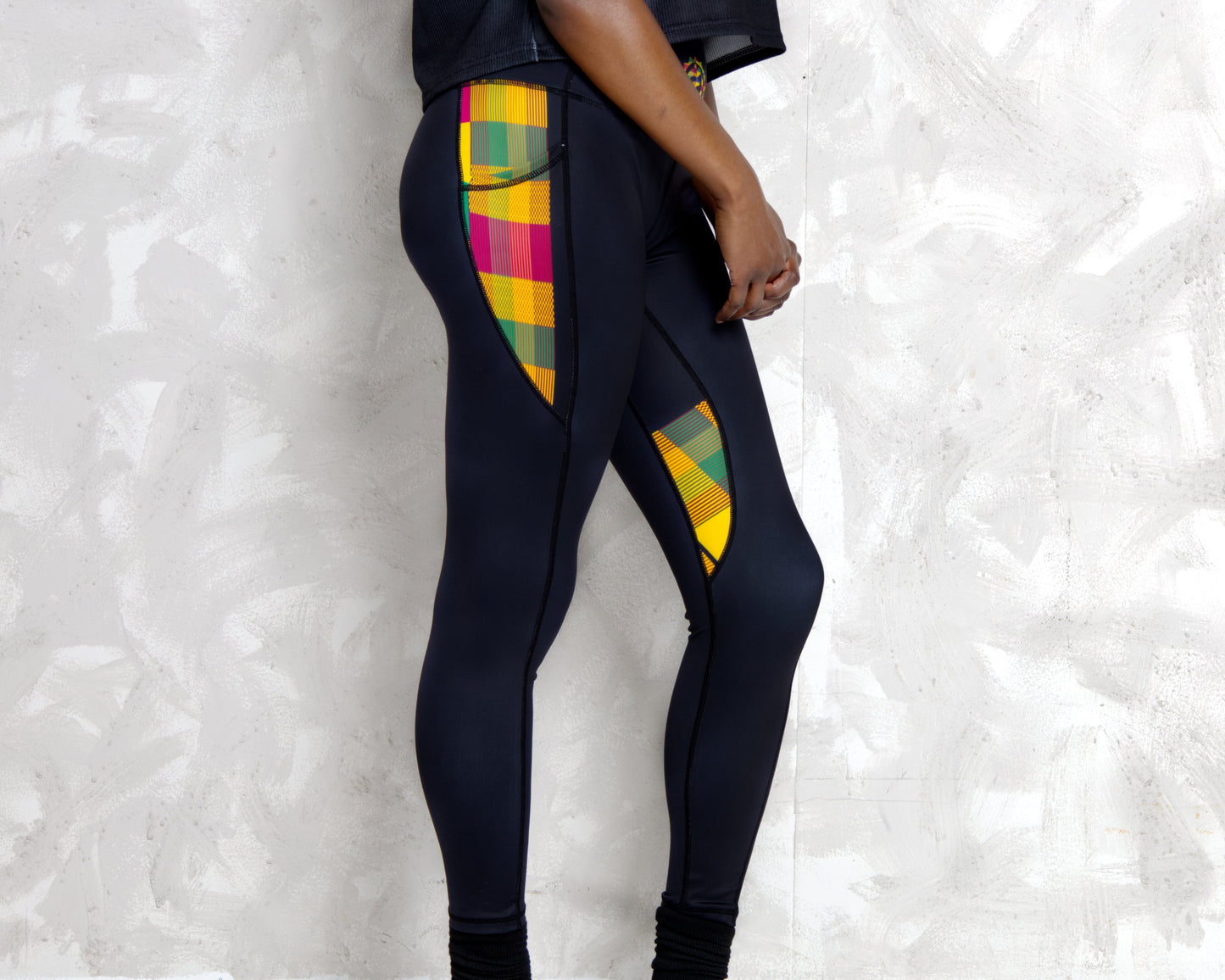 Person wearing black leggings with colorful Kente patterns on a light gray background