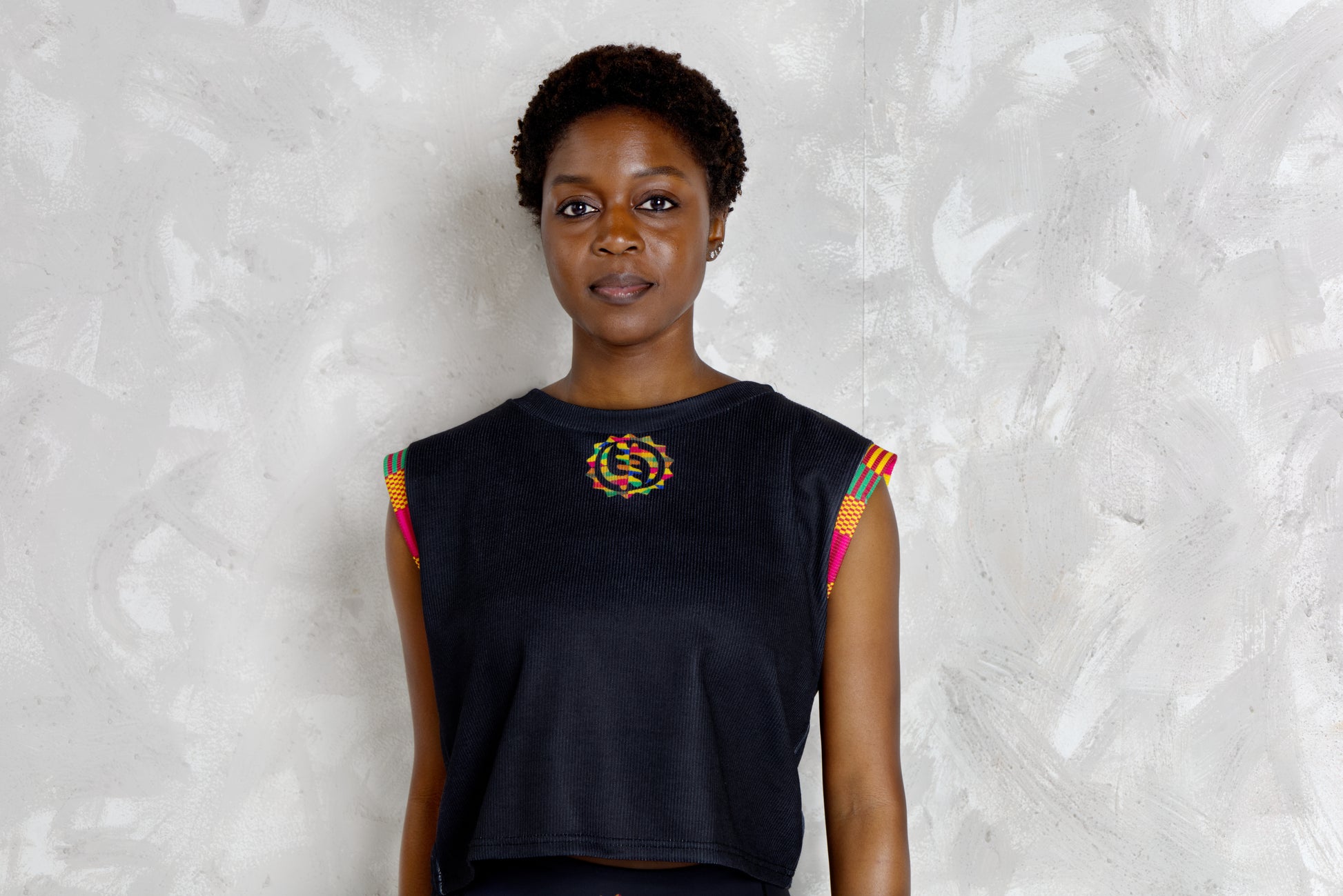Woman wearing a black sleeveless top with colorful kente patterns on a textured white background