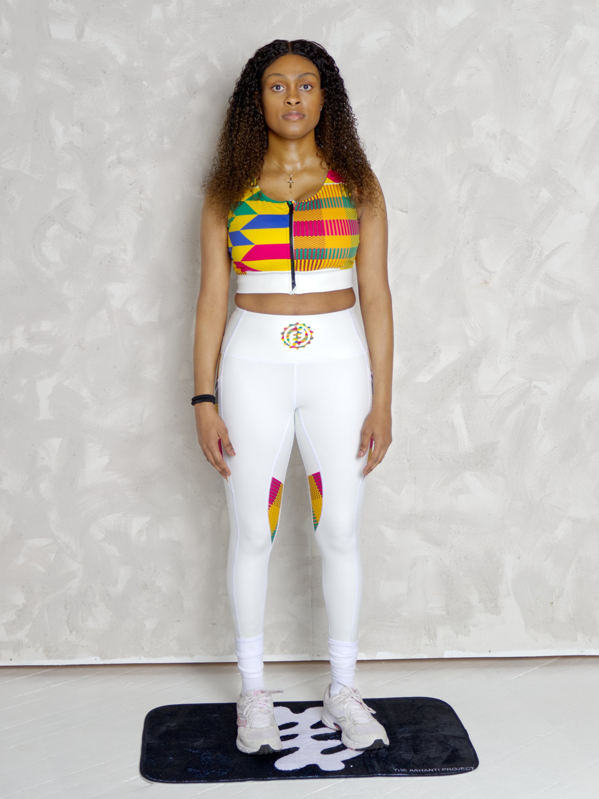 Person wearing a colorful top and white leggings with a rainbow design on a plain background
Black woman wearing white leggings with colorful kente designs on a plain background. Athletic wear. Gym outfit, 