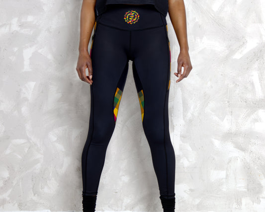 Person wearing black leggings with colorful Kente accents against a textured white wall.