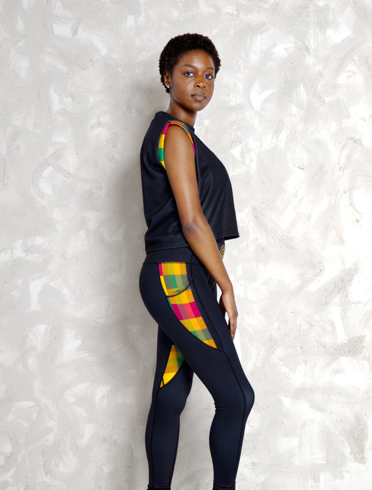 Person wearing a black outfit with colorful Kente patterns against a textured white wall.