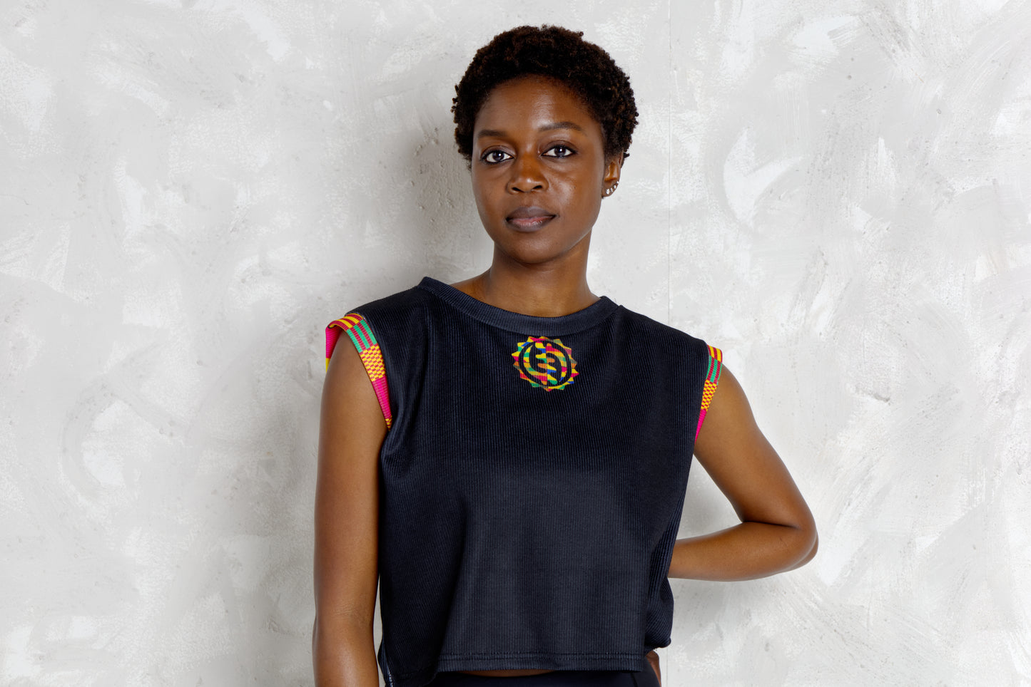 Woman wearing a black sleeveless top with colorful kente patterns on a textured white background