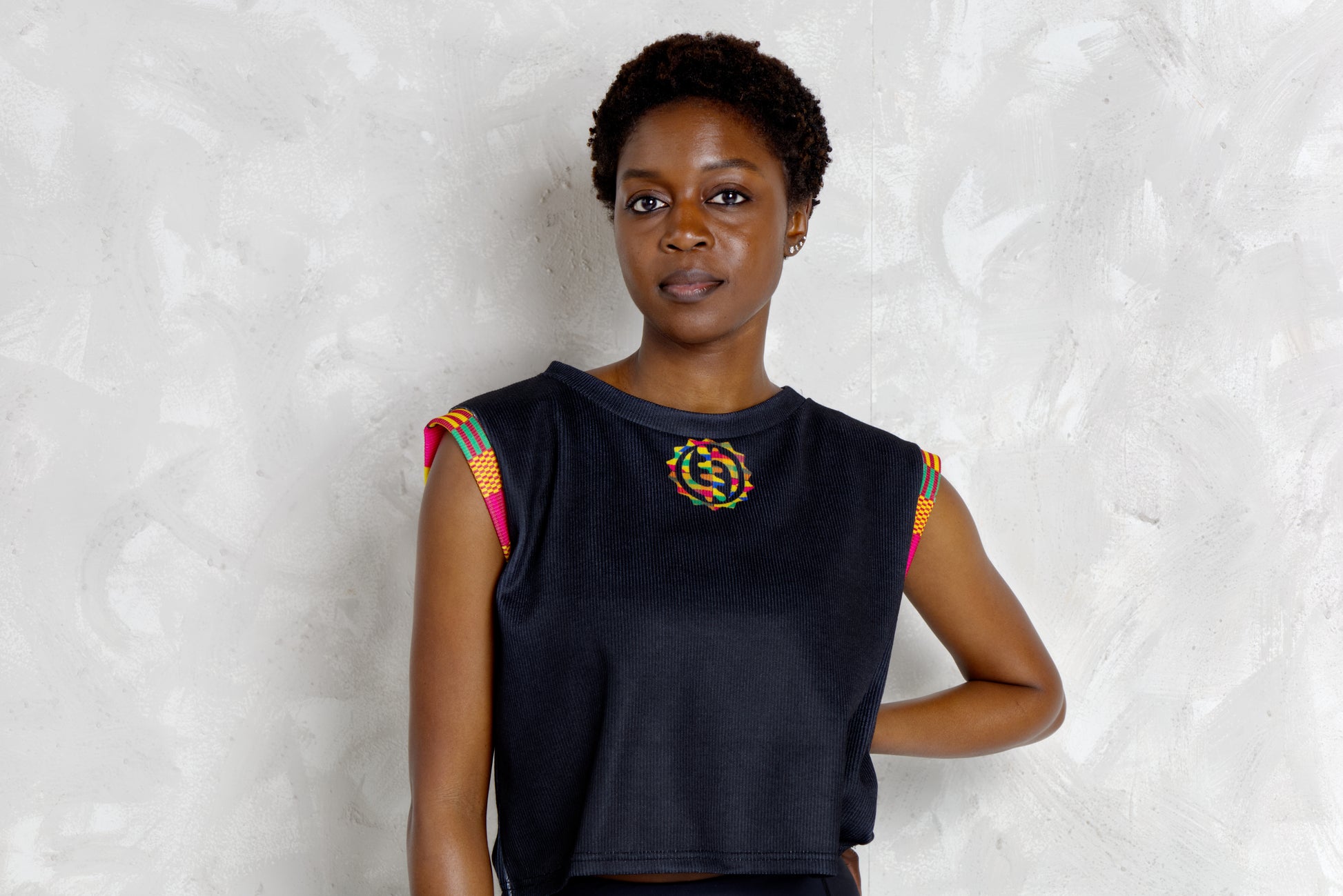 Woman wearing a black sleeveless top with colorful kente patterns on a textured white background