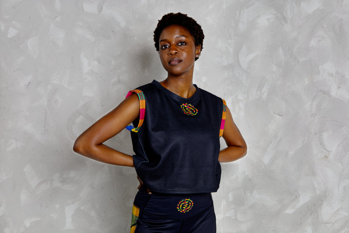 Woman wearing a black sleeveless top with colorful kente patterns on a textured white background