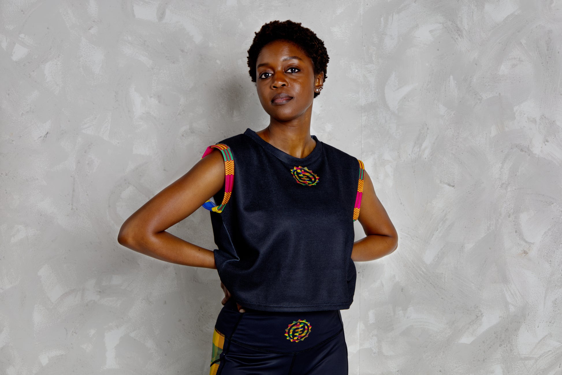 Woman wearing a black sleeveless top with colorful kente patterns on a textured white background