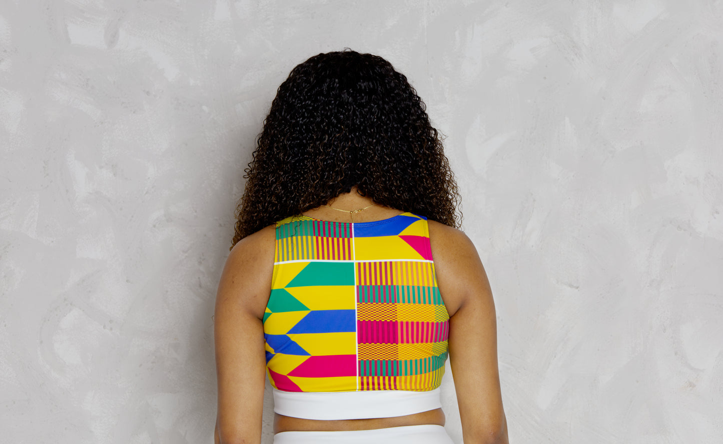 Woman wearing a colorful patterned top against a gray background
Woman wearing a colorful kente patterned top against a plain background. It’s a padded sports bra with kente designs 