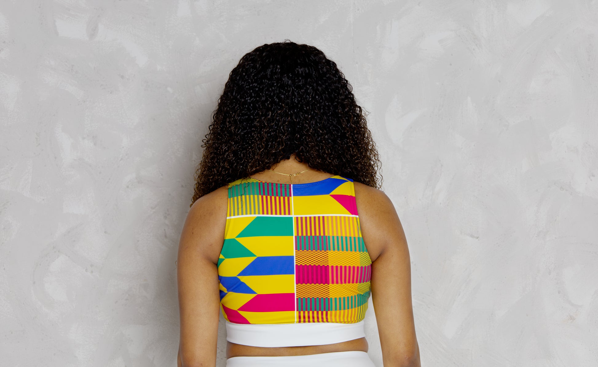 Woman wearing a colorful patterned top against a gray background
Woman wearing a colorful kente patterned top against a plain background. It’s a padded sports bra with kente designs 