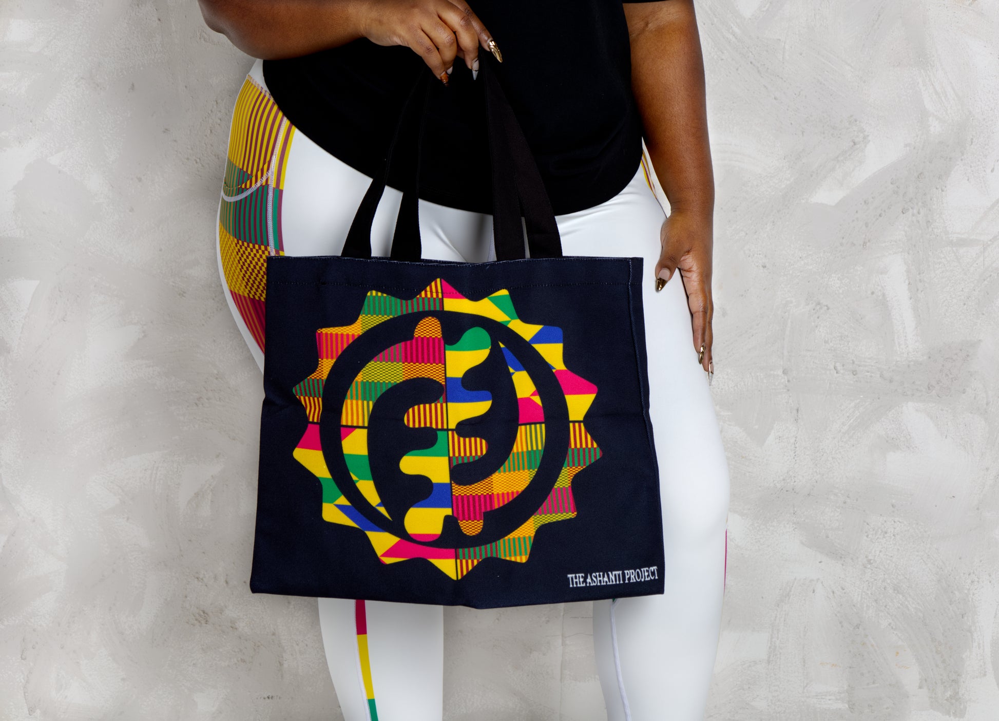 Black person holding a tote bag with a colorful design and text on a light gray background