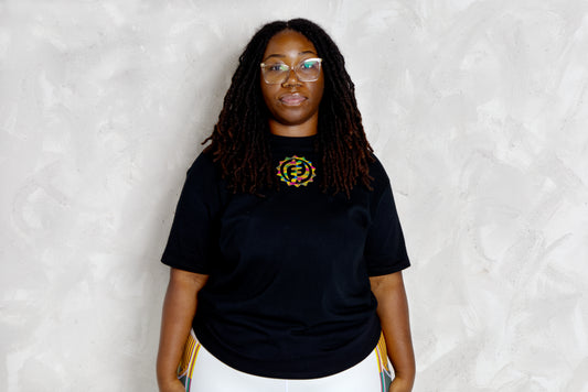 Person wearing a black t-shirt with a kente logo against a white background